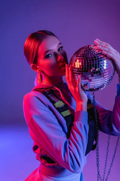 Mujer joven y elegante sosteniendo brillante bola disco en púrpura - foto de stock