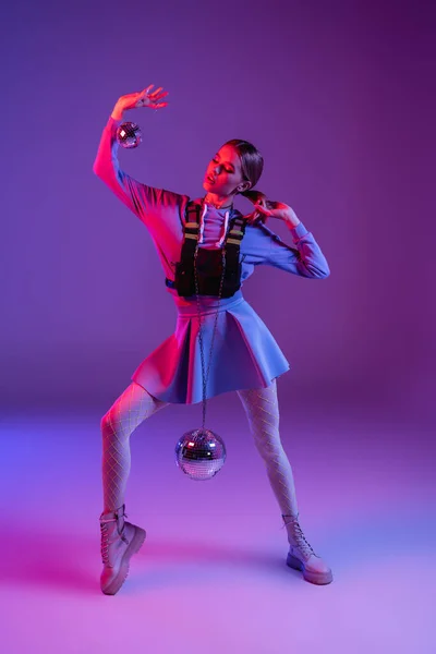 Volle Länge der modischen Frau im Rock hält Discokugeln, während sie auf lila posiert — Stockfoto