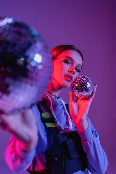 Stylish woman in skirt holding disco balls on blurred foreground and purple background — Stock Photo