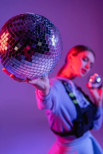 Festa bola de discoteca na mão de mulher na moda no fundo roxo e borrado — Fotografia de Stock