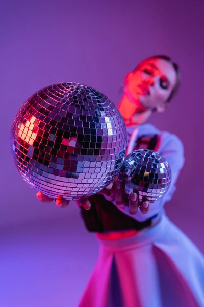 Bolas de discoteca brilhantes nas mãos da mulher na moda no fundo roxo e borrado — Fotografia de Stock