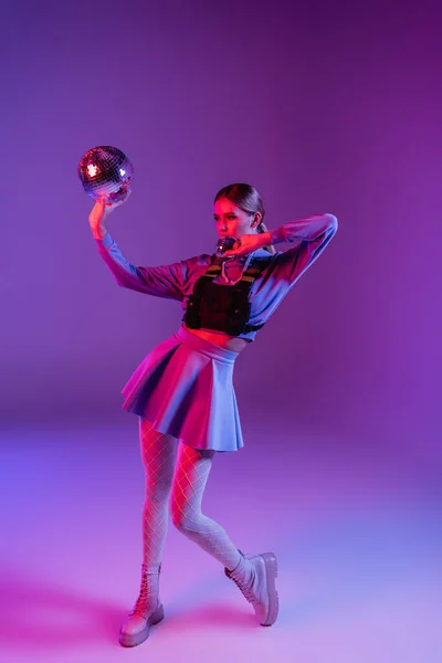 Pleine longueur de femme à la mode en jupe tenant des boules de disco sur violet — Photo de stock