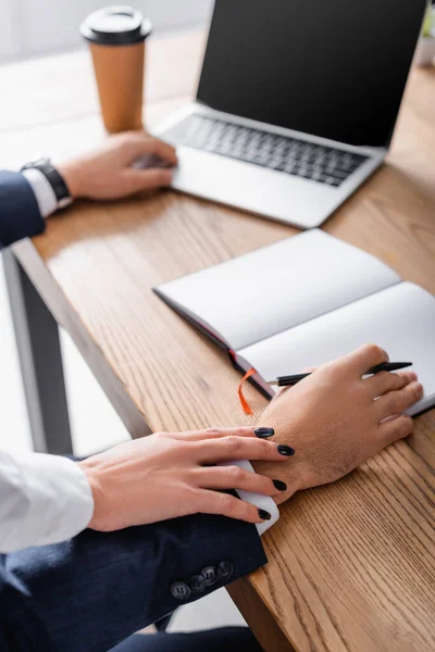 Vue recadrée du secrétaire touchant la main d'un homme d'affaires près d'un ordinateur portable et portable, fond flou — Photo de stock