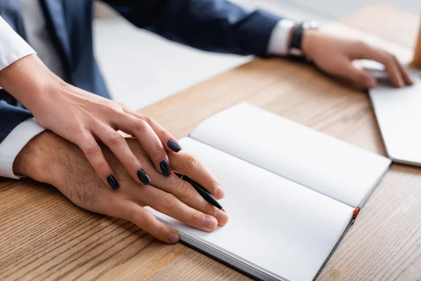 Abgeschnittene Ansicht der Geschäftsfrau, die Hand eines Kollegen in der Nähe eines leeren Notizbuchs auf dem Schreibtisch berührt, verschwommener Hintergrund — Stockfoto