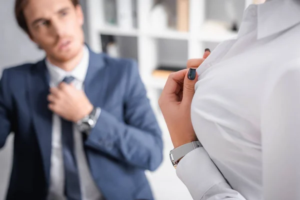 Сексуальна бізнес-леді розстібає блузку біля бізнесмена, торкаючись краватки на розмитому фоні — стокове фото