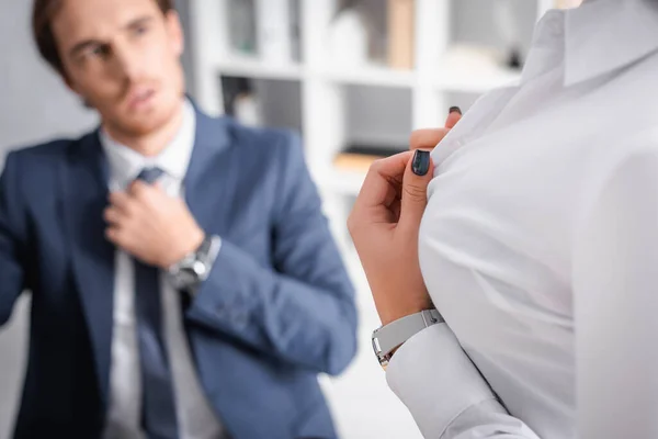 Sexy mujer de negocios desabotonamiento blusa cerca de hombre de negocios tocando corbata sobre fondo borroso - foto de stock