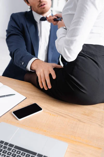Vista recortada de la mujer de negocios sentada en el escritorio mientras seduce a su colega en la oficina - foto de stock