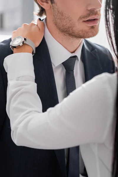 Vista recortada de hombre de negocios coqueteando con colega y tocándose el hombro en la oficina, borrosa primer plano - foto de stock