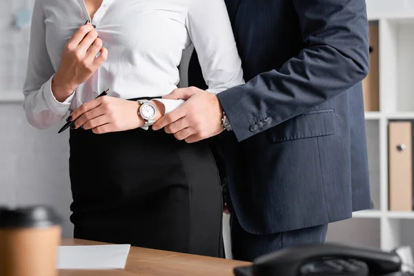 Partial view of businessman touching hand of sensual secretary unbuttoning blouse, blurred foreground — Stock Photo