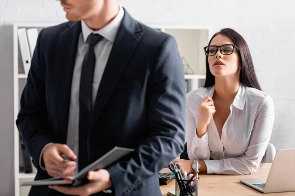 Seductive businesswoman at workplace looking at colleague holding notebook on blurred foreground — Stock Photo