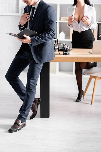 Cropped view of seductive businesswoman unbuttoning blouse near businessman standing with notebook — Stock Photo