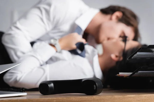 Selective focus of phone handset near businessman kissing secretary on blurred background — Stock Photo