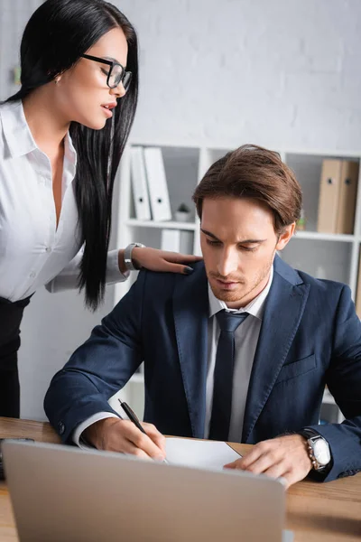 Sensuelle brunette femme d'affaires touchant épaule de l'homme d'affaires tout en le séduisant au bureau, flou au premier plan — Photo de stock