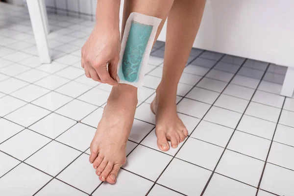Teilansicht einer Frau, die Wachsstreifen am Bein im Badezimmer entfernt — Stockfoto