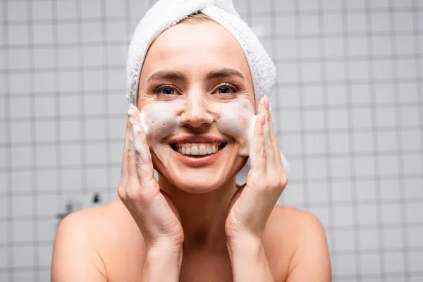 Mujer feliz con hombros desnudos aplicando limpiador de espuma en el baño - foto de stock