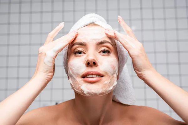 Femme aux épaules nues appliquant un nettoyant mousse dans la salle de bain — Photo de stock