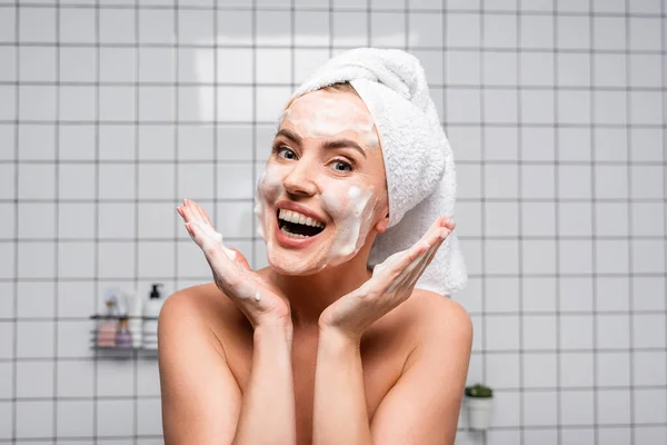 Femme excitée avec des épaules nues appliquer un nettoyant mousse dans la salle de bain — Photo de stock