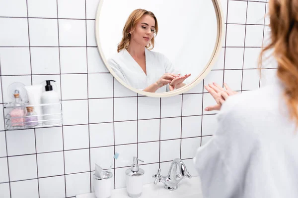 Mujer aplicando crema de manos cerca del espejo en el baño - foto de stock
