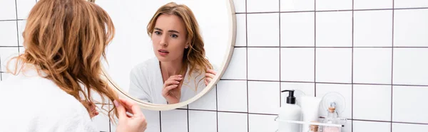 Donna sconvolta in accappatoio che regola i capelli guardando lo specchio in bagno, banner — Foto stock