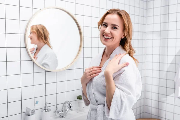 Mujer alegre en albornoz sonriendo en el baño - foto de stock