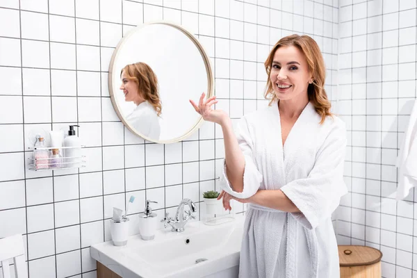 Fröhliche Frau im Bademantel lächelt, während sie im Badezimmer gestikuliert — Stockfoto