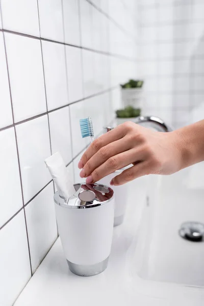 Vista recortada de la mujer tomando cepillo de dientes en el baño - foto de stock