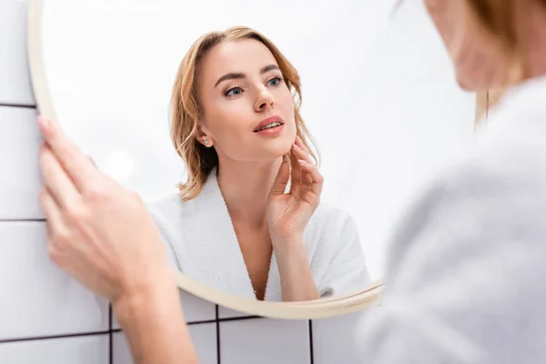 Жінка дивиться на дзеркало і торкається обличчя у ванній — стокове фото