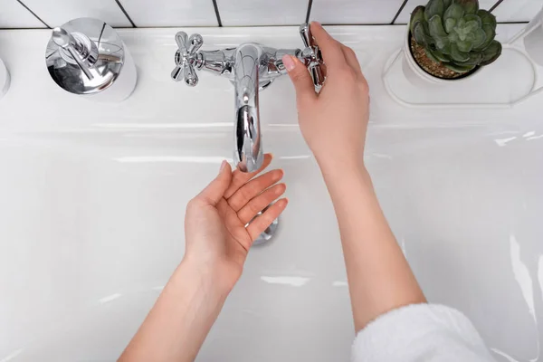 Top view of woman opening faucet near soap dispenser and plant in bathroom — Stock Photo