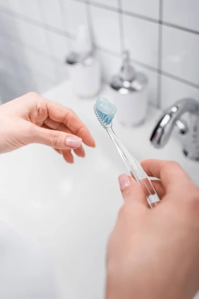Обрезанный вид женщины, держащей зубную щетку с зубной пастой возле раковины — стоковое фото