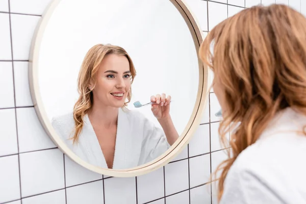 Щаслива жінка тримає зубну щітку з зубною пастою біля дзеркала — стокове фото