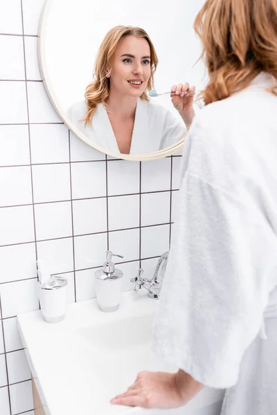 Donna allegra che tiene lo spazzolino da denti con dentifricio e si guarda allo specchio — Foto stock