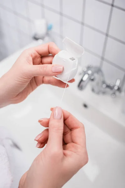 Vue recadrée de la femme tenant récipient en plastique avec fil dentaire dans la salle de bain — Photo de stock
