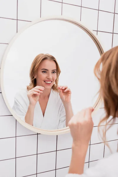 Glückliche Frau blickt in den Spiegel und hält Zahnseide in der Hand — Stockfoto