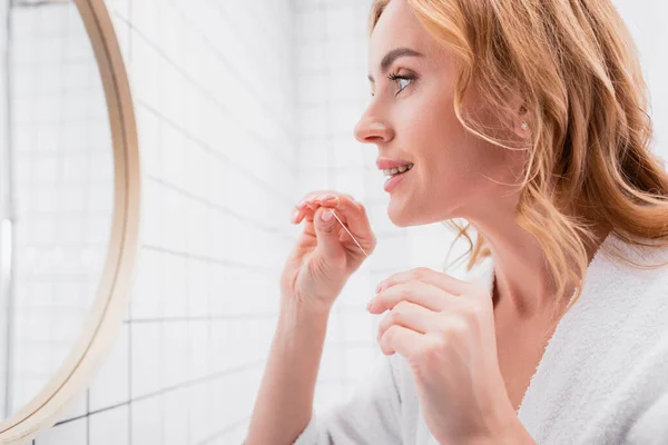 Cheerful woman looking at mirror and holding dental floss — Stock Photo