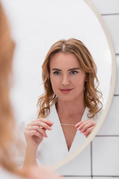 Spiegelbild einer fröhlichen Frau, die in den Spiegel schaut und Zahnseide in der Hand hält — Stockfoto