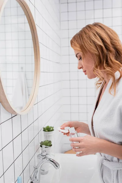 Женщина держит бутылку с тонером и хлопка площадку в ванной комнате — стоковое фото