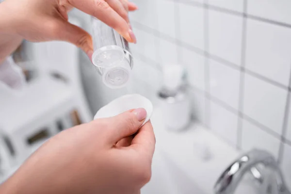 Teilansicht einer Frau, die eine Flasche mit Toner und Wattepad im Badezimmer hält — Stockfoto