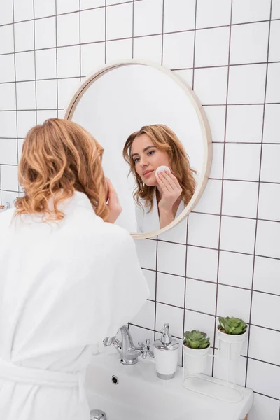 Femme heureuse appliquant du toner sur le visage avec du coton et regardant miroir — Photo de stock