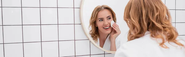 Frau trägt Toner mit Wattepad im Gesicht auf und blickt in Spiegel, Banner — Stockfoto