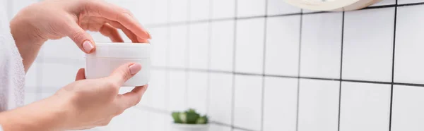 Vista ritagliata della donna che tiene il vaso con la crema per il viso in bagno, banner — Foto stock