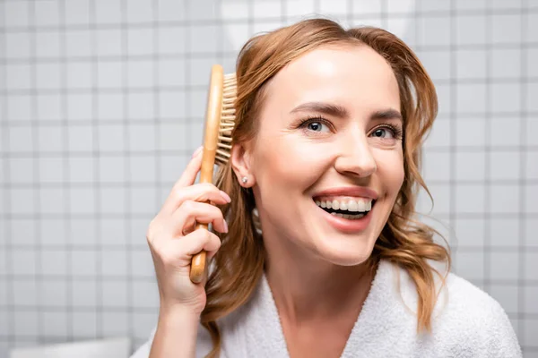 Glückliche Frau lächelt und bürstet Haare im Badezimmer — Stockfoto