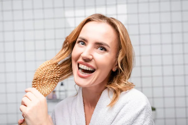 Freudige Frau lächelt und bürstet Haare im Badezimmer — Stockfoto