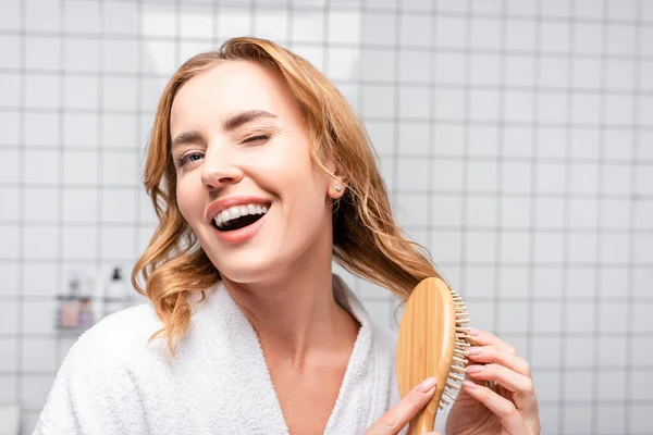 Freudige Frau lächelt und zwinkert beim Haareputzen im Badezimmer — Stockfoto