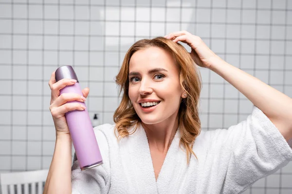 Весела жінка тримає пляшку з спреєм для волосся у ванній — стокове фото