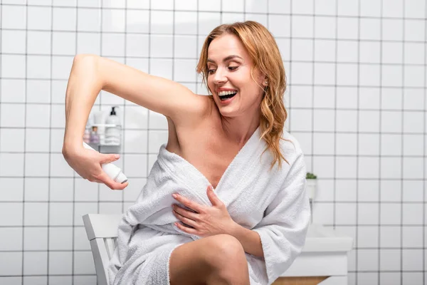 Mulher alegre em toalha branca aplicando spray desodorante no banheiro — Fotografia de Stock