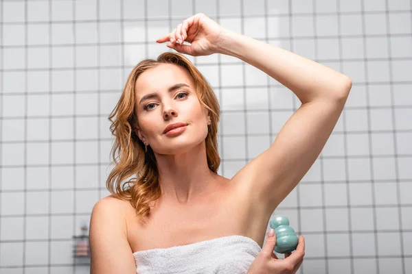 Woman in white towel applying deodorant roll  in bathroom — Stock Photo