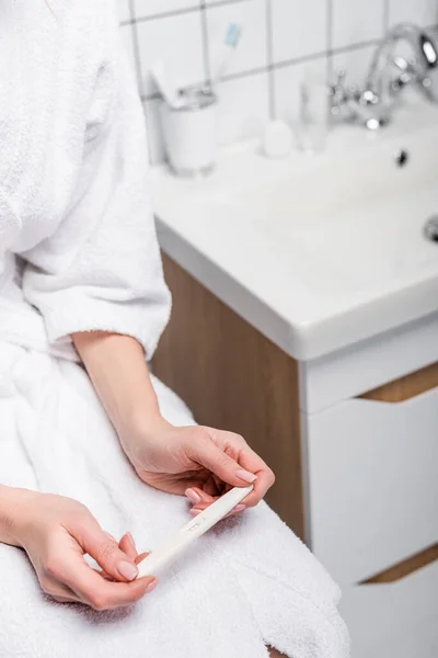 Cropped view of woman in bathrobe holding pregnancy test in bathroom — Stock Photo