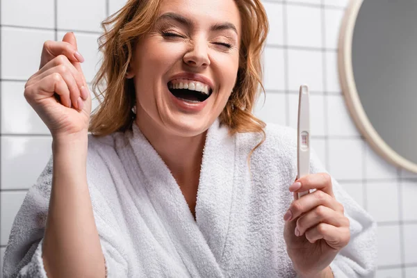 Mujer alegre en albornoz blanco celebración de prueba de embarazo en el baño - foto de stock