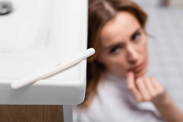 Pregnancy test with positive result near worried woman on blurred background — Stock Photo