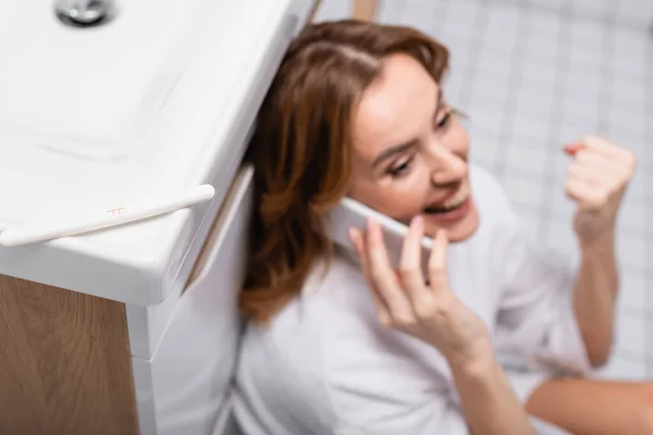 Test di gravidanza con esito positivo vicino a donna felice che parla su smartphone su sfondo sfocato — Foto stock